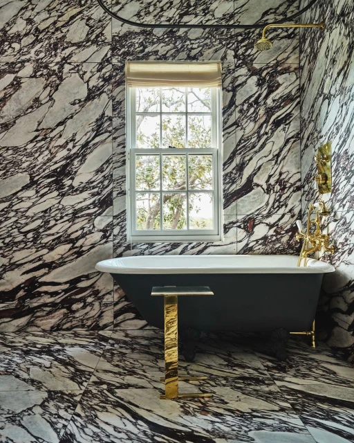 Bathroom featuring a freestanding tub, gold accents, and marble walls, creating an elegant and luxurious interior space.
