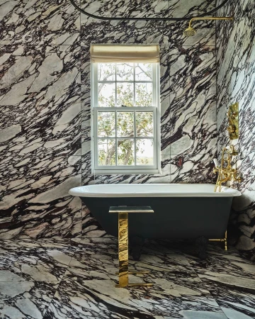 Bathroom featuring a freestanding tub, gold accents, and marble walls, creating an elegant and luxurious interior space.