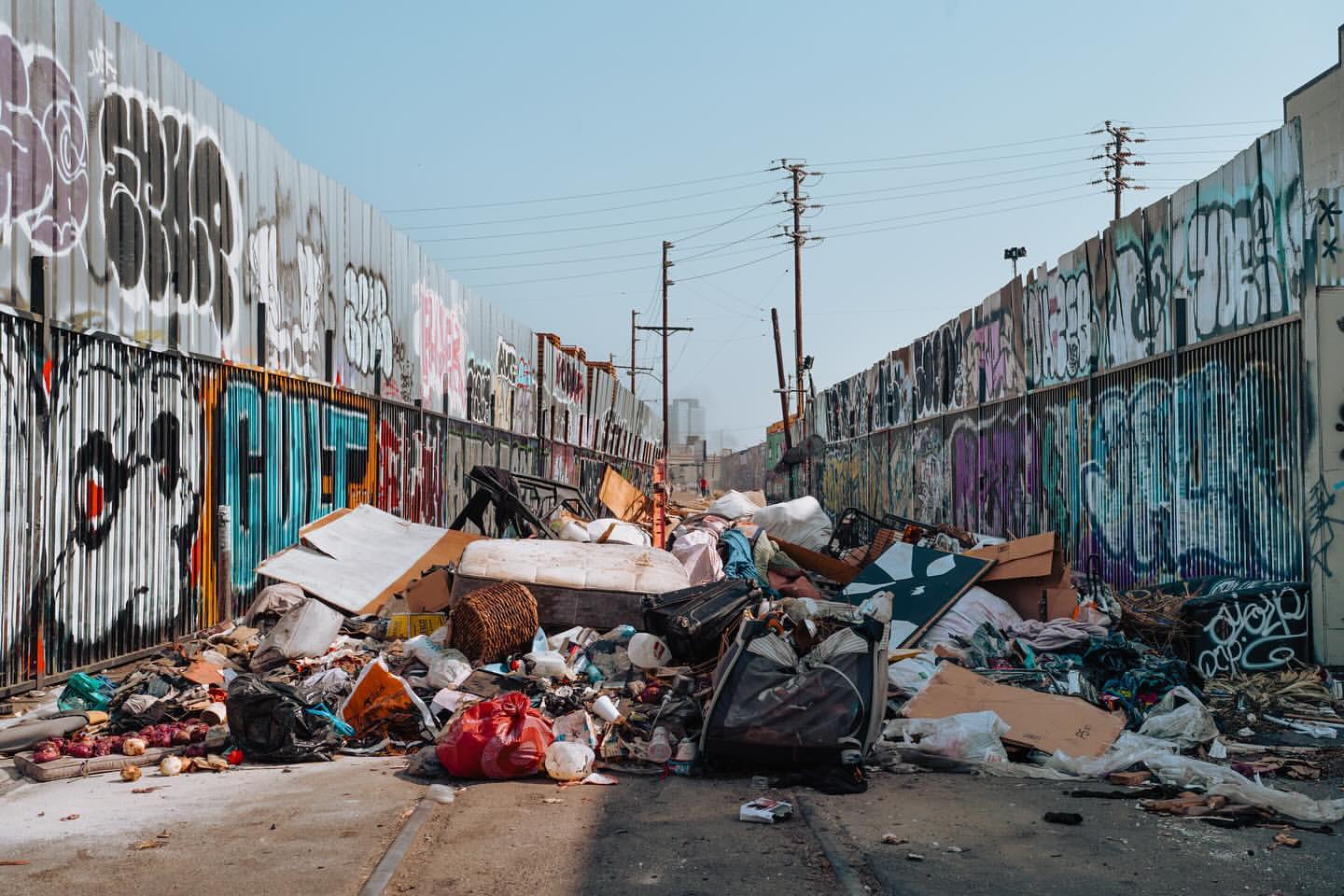 Urban decay shows a garbage pile on a street next to graffiti-covered walls under a clear sky, representing environmental neglect.