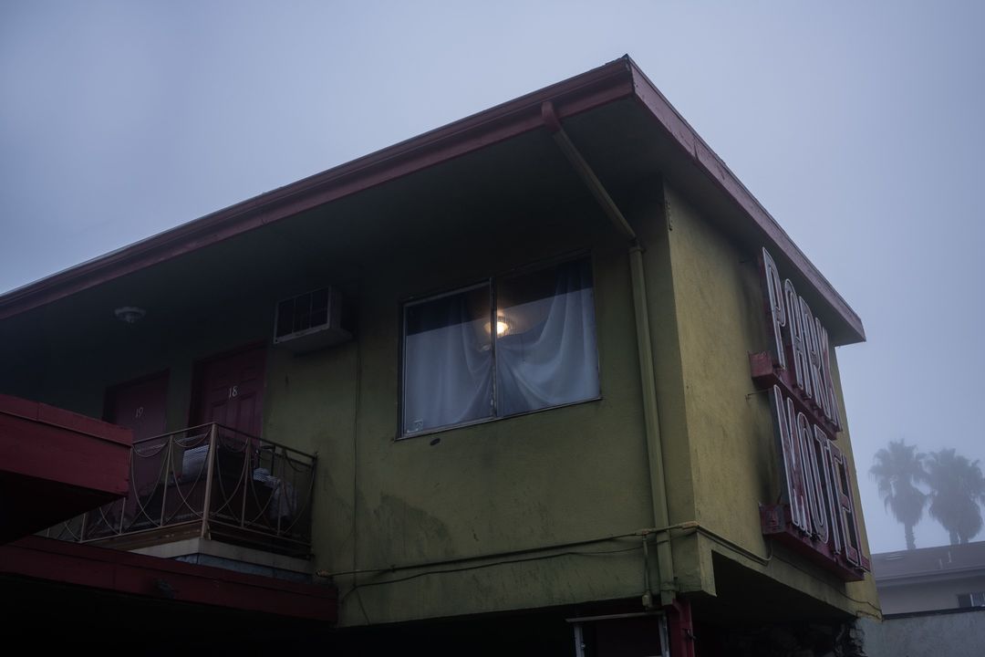 Exterior view of a yellow and red two-story motel building under a foggy sky, featuring a balcony, windows, and visible signage.