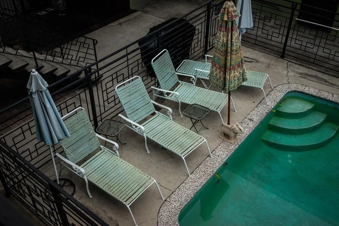 High angle view of a swimming pool terrace with several pale green lounge chairs, umbrellas, and metal railings.