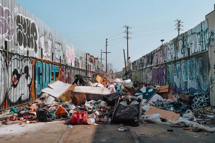 An alleyway flanked by corrugated metal walls covered in graffiti, with a large pile of debris blocking the path.