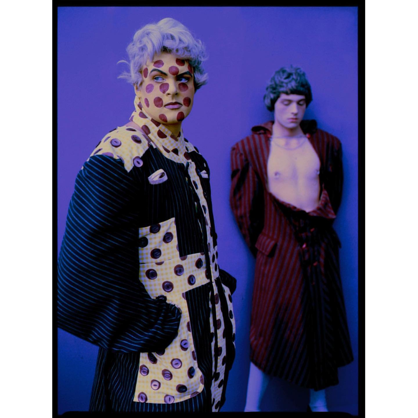 Two people in sculptural patterned garments against a solid blue backdrop photographed by Perry Ogden