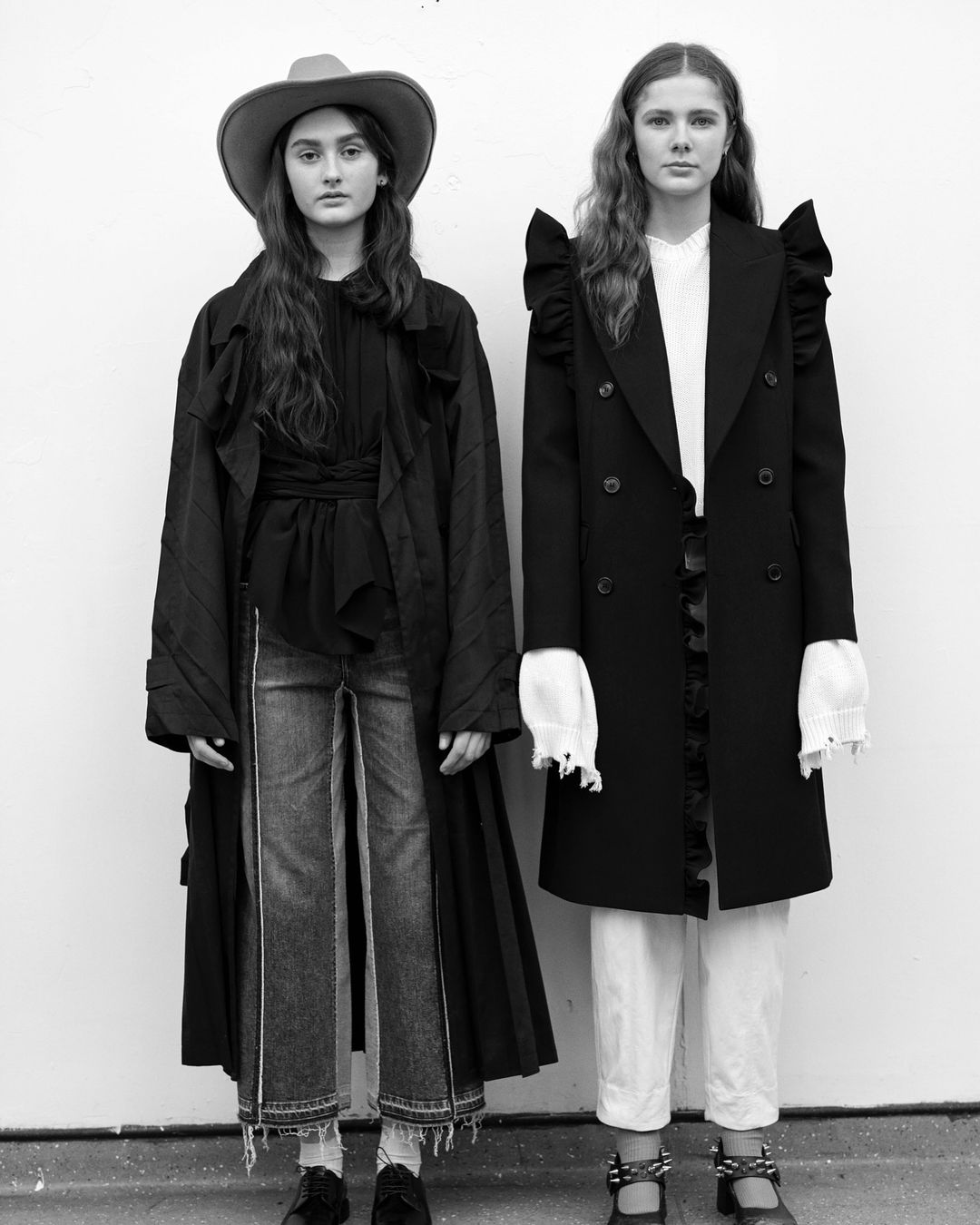 Two fashion models in a black and white shot. One wears a cowboy hat, while both are dressed in ruffled outerwear and denim. 