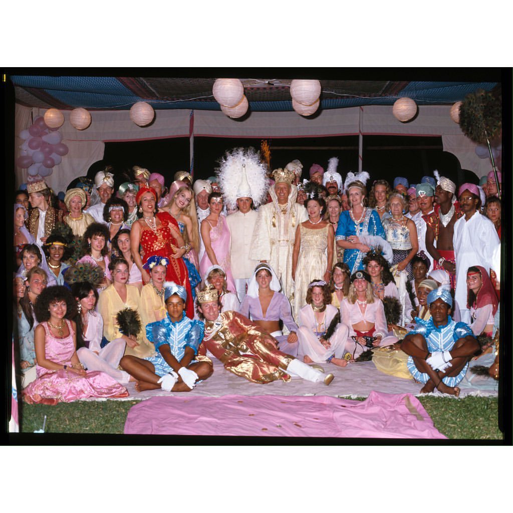 Large group of people dressed in costumes with headdresses gather outdoors under tents with paper lanterns for a festive occasion.