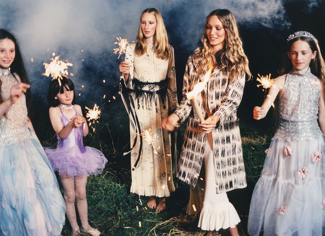Five children and adult women in dresses pose with sparklers outdoors at night, creating a whimsical and celebratory scene.