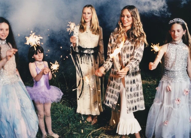 Five children and adult women in dresses pose with sparklers outdoors at night, creating a whimsical and celebratory scene.