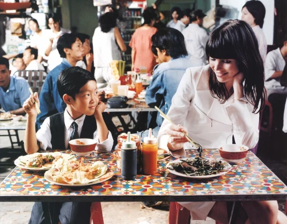 A young boy and a woman eating at a colorful tiled table in a busy restaurant, photographed by Perry Ogden.