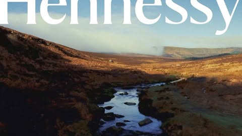 Scenic landscape of a river flowing through a valley with hills, and Hennessy text overlayed at the top of the image.