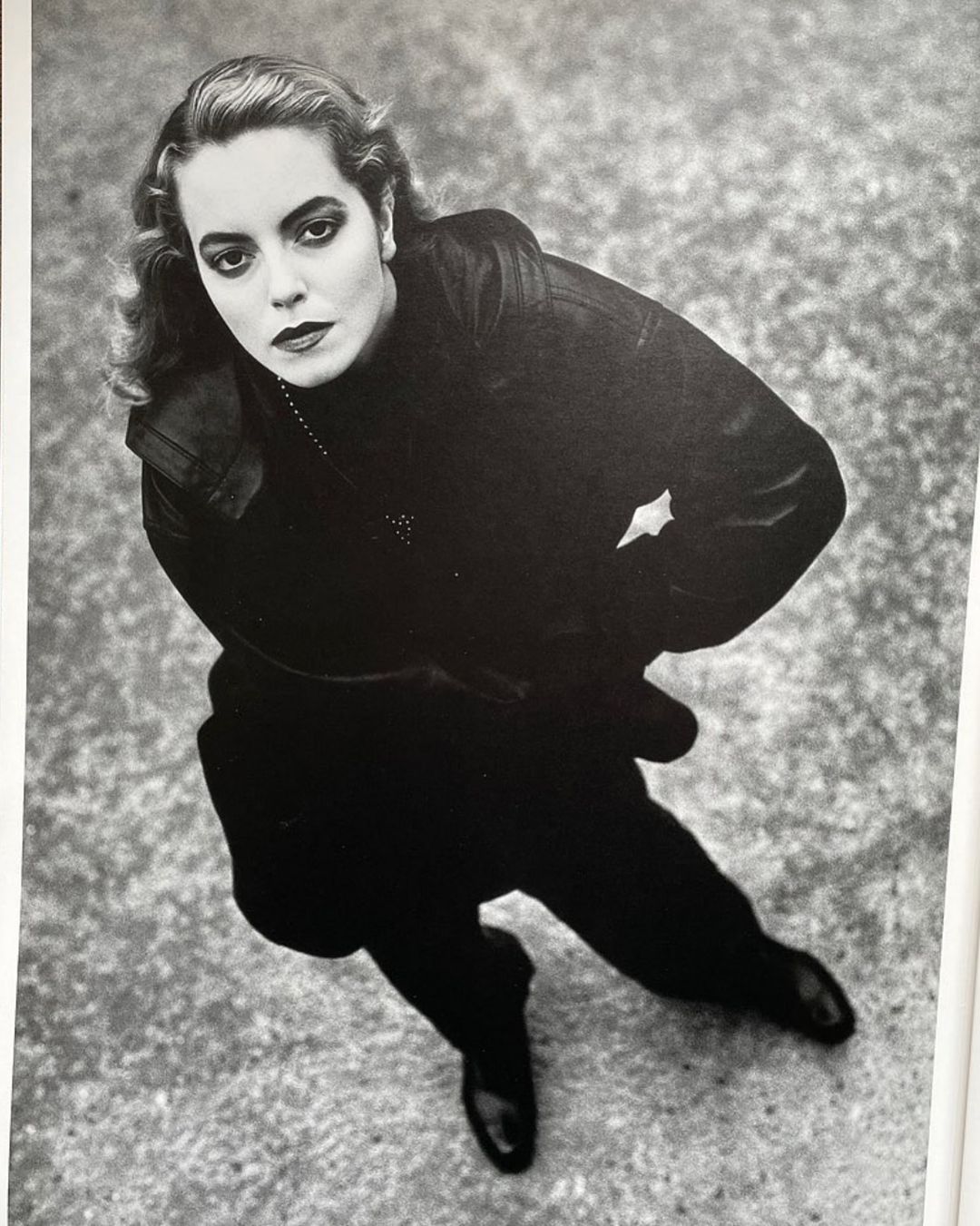 Monochrome portrait of a woman in dark clothing, shot from a high angle against a textured gray background with a slight tilt.