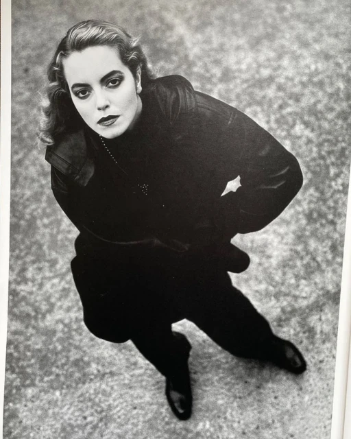 Monochrome portrait of a woman in dark clothing, shot from a high angle against a textured gray background with a slight tilt.