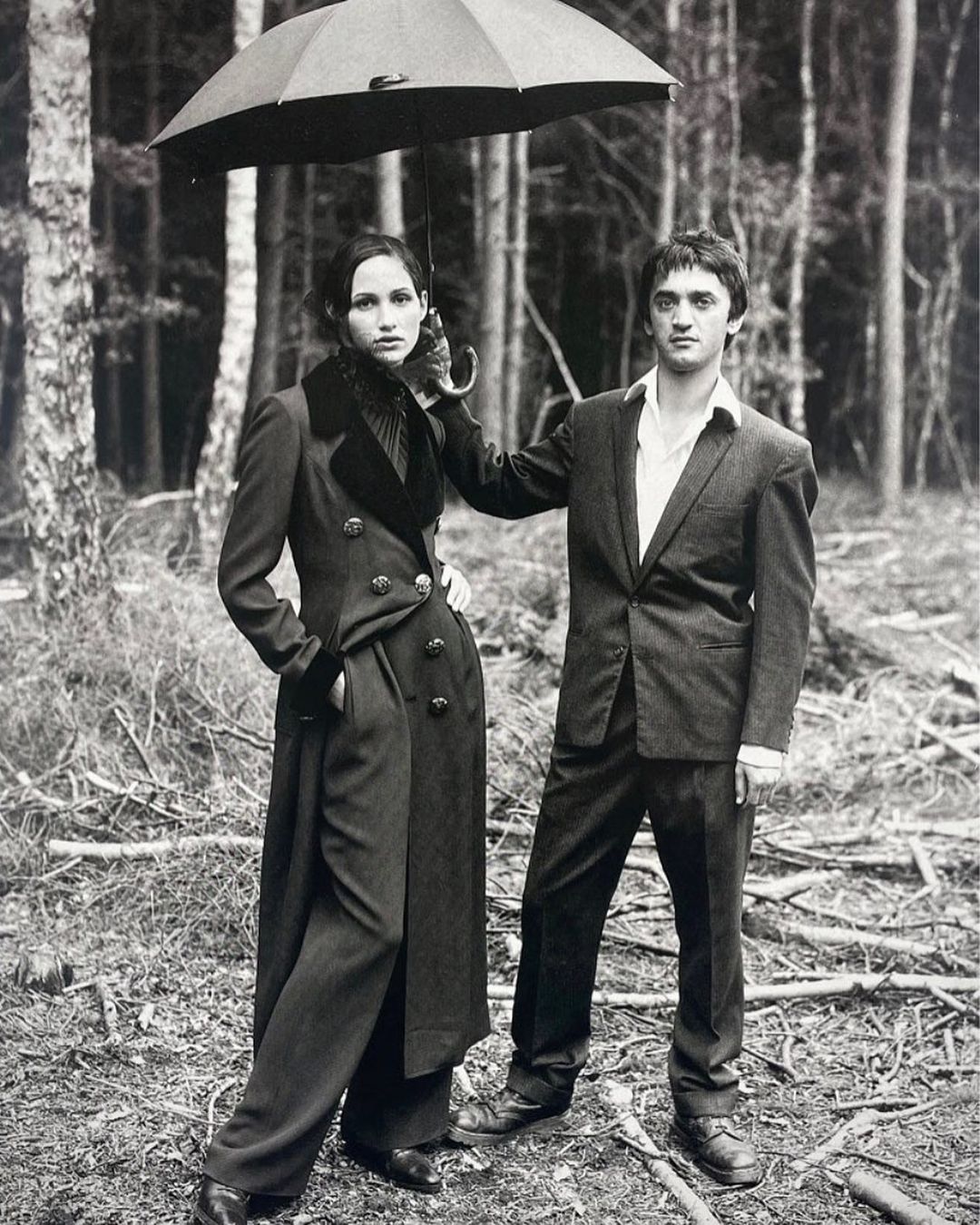Monochrome fashion portrait of a stylish couple with a black umbrella, posing in a wooded area.