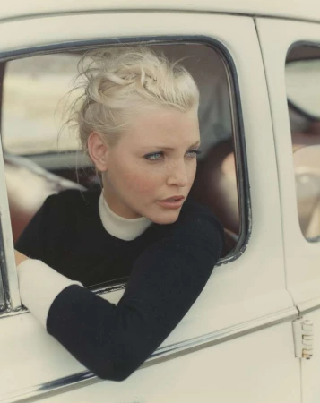 Blonde woman in a black top looking out the window of a vintage white car