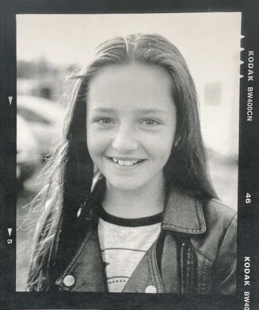 Black and white portrait of a smiling young girl with long dark hair wearing a leather jacket, framed by film border negatives.