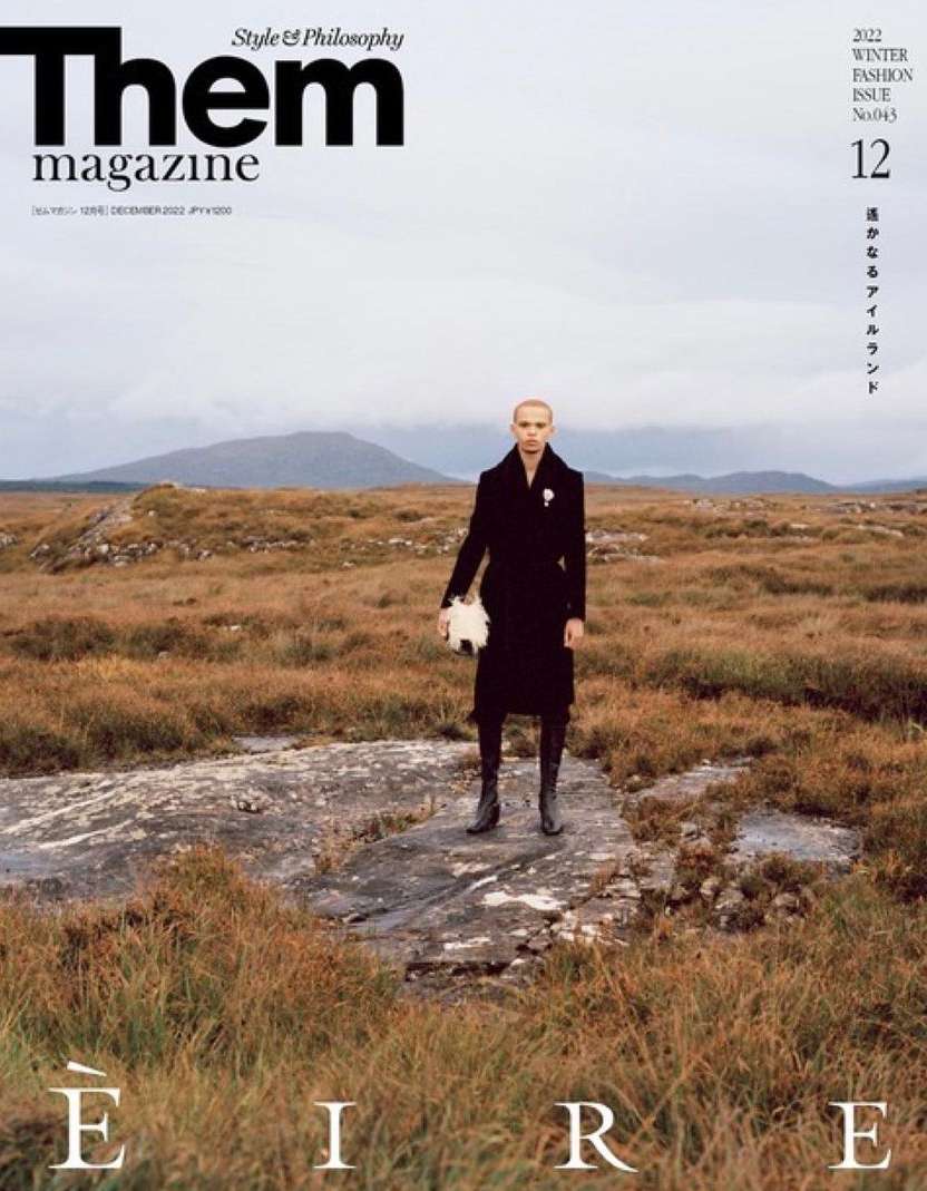 Them magazine cover featuring a person in a black coat standing in a field, with text overlay and mountain backdrop.