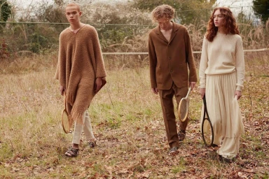 Three models holding vintage tennis rackets walking through a grassy meadow wearing brown and cream knitwear by Perry Ogden.
