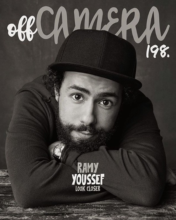 Monochrome portrait of Ramy Youssef wearing a cap, resting his arms on a wooden surface, with 'off CAMERA 198.' text above him.
