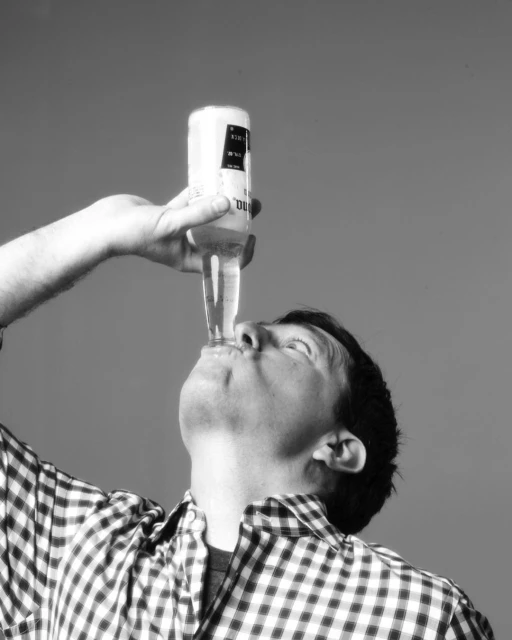 Man drinking Corona beer in black and white. The beer bottle is tilted upward, and the person is taking a sip in an indoor environment.