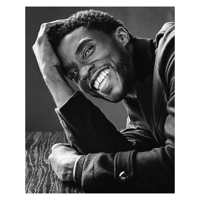 Black and white portrait of Chadwick Boseman smiling with his hand to his head, photographed by Sam Jones
