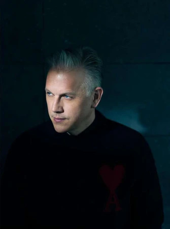Studio portrait of a mature adult male with silver hair wearing a black sweater, looking off to the side, against a dark gray background.
