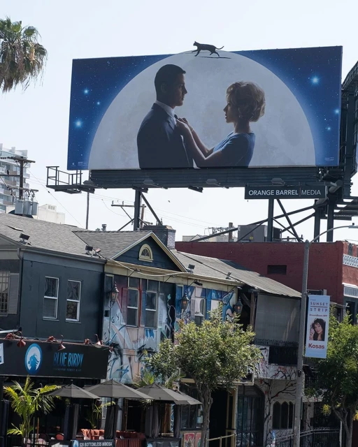 Billboard featuring a couple and a large moon in an urban setting, juxtaposed with buildings and clear sky, showcasing outdoor advertising.