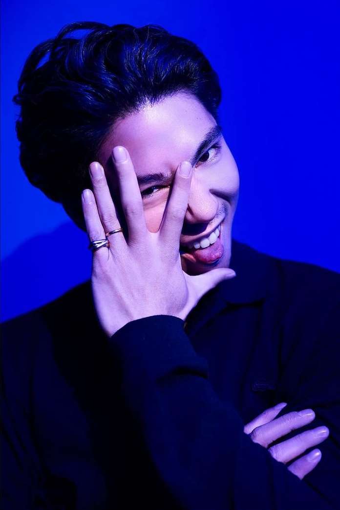 Close-up portrait of a man holding his hand up to his face and smiling against a vibrant blue background
