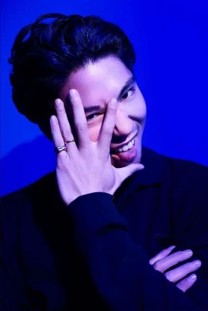 Close-up portrait of a man holding his hand up to his face and smiling against a vibrant blue background