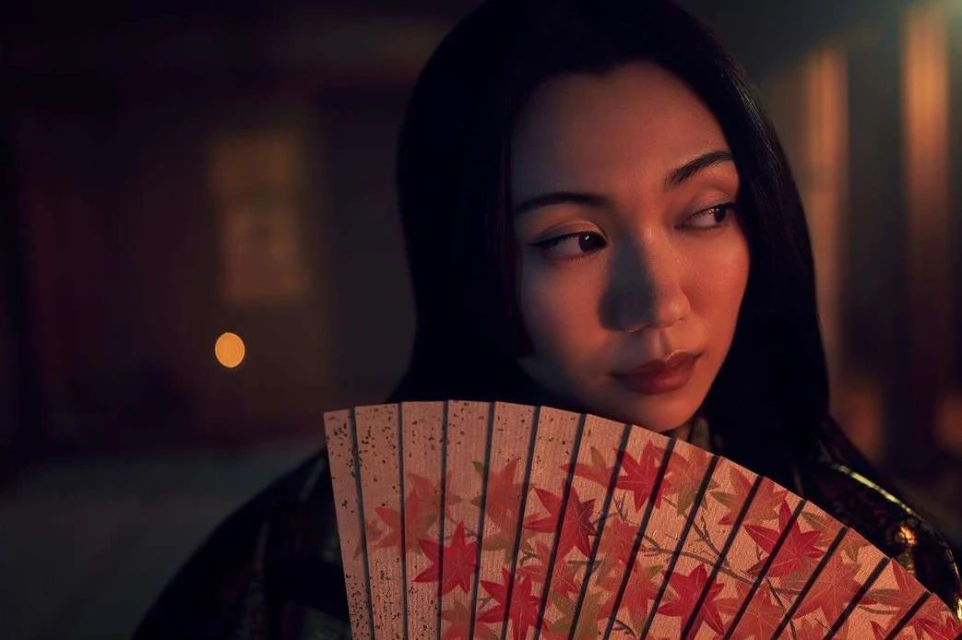 Portrait of a woman holding a fan with maple leaf patterns in a dimly lit indoor environment. The woman is looking to the side.