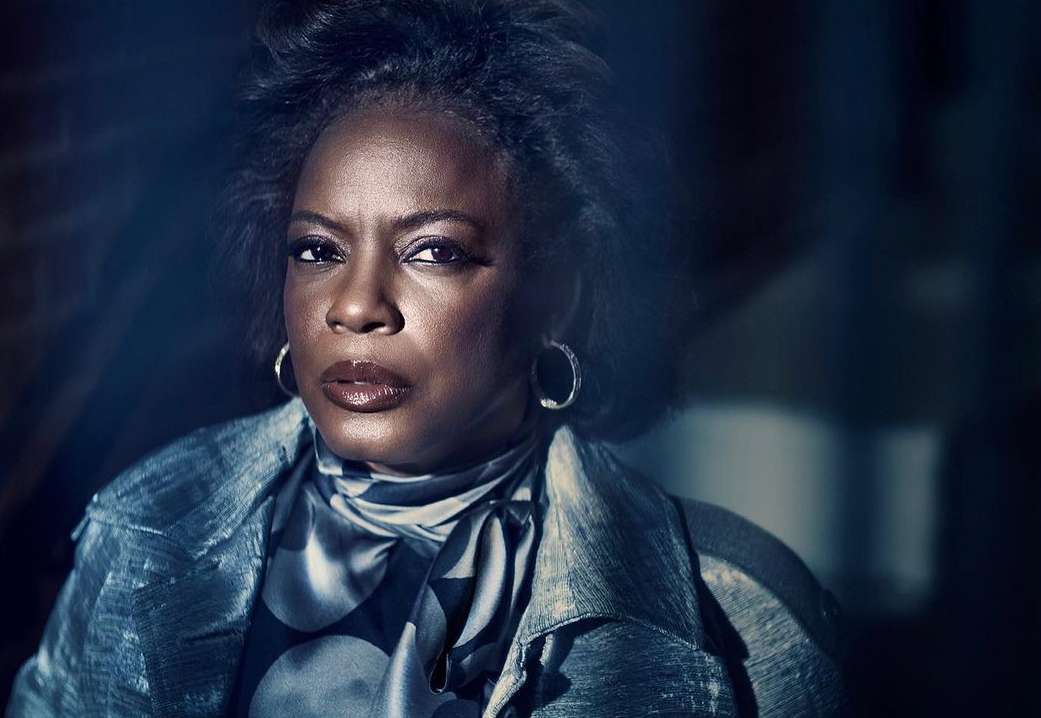 Close-up portrait of an adult female of African descent with short dark hair, wearing silver hoop earrings, a patterned scarf, and a coat.
