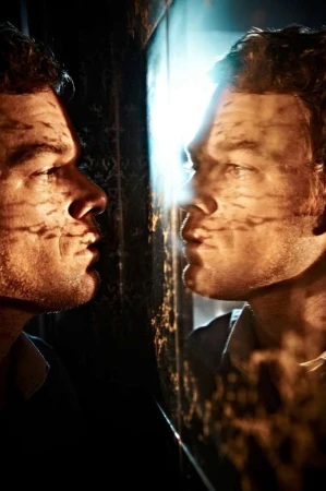 Portrait of Michael C. Hall reflected in a mirror with dappled shadow patterns cast across his face, photographed by Kurt Iswarienko.