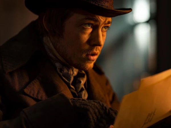 Close up of a man in a hat and coat reading documents, set indoors with warm lighting and a slightly concerned facial expression.