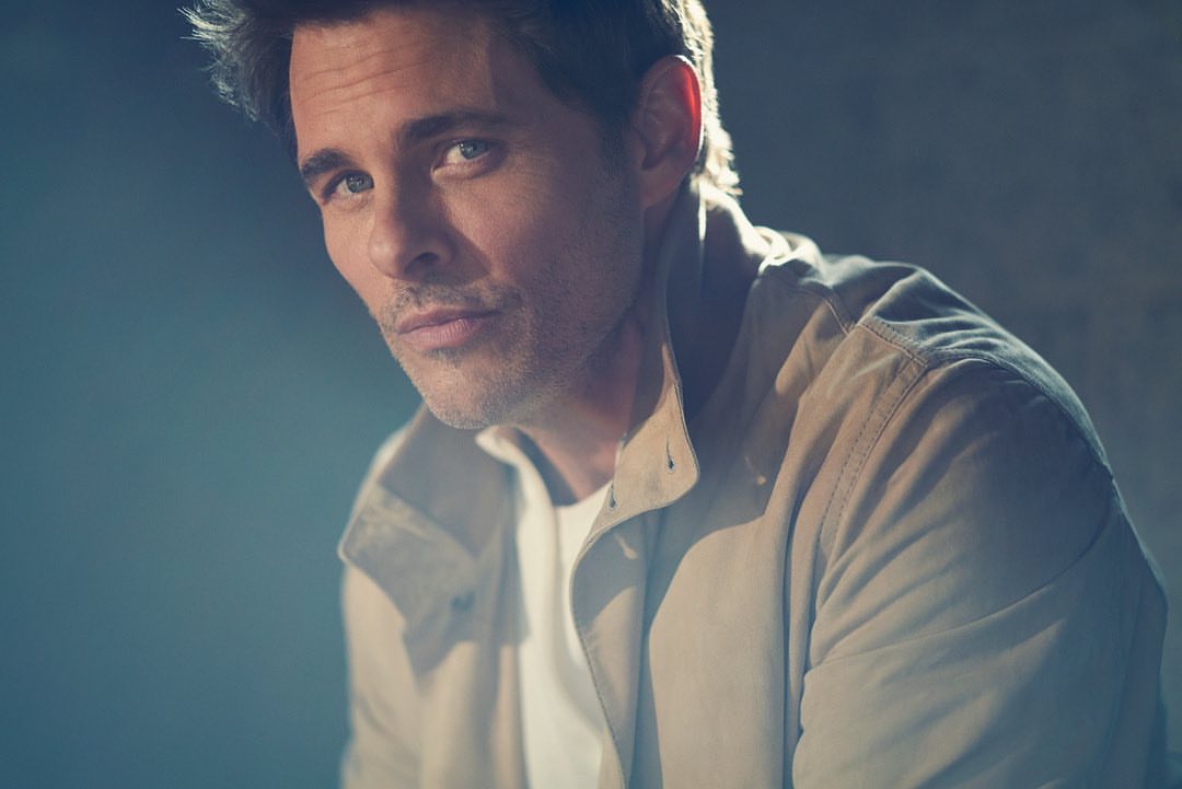 Close-up studio shot of a fair-skinned adult male in a white T-shirt and beige jacket, looking at the camera with a neutral expression.