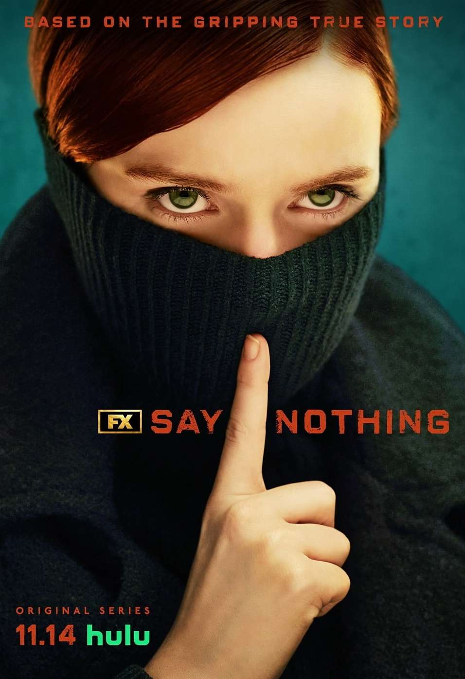 Close-up of a woman with red hair wearing a black turtleneck covering her mouth and nose, holding a finger to her lips in a studio shot.