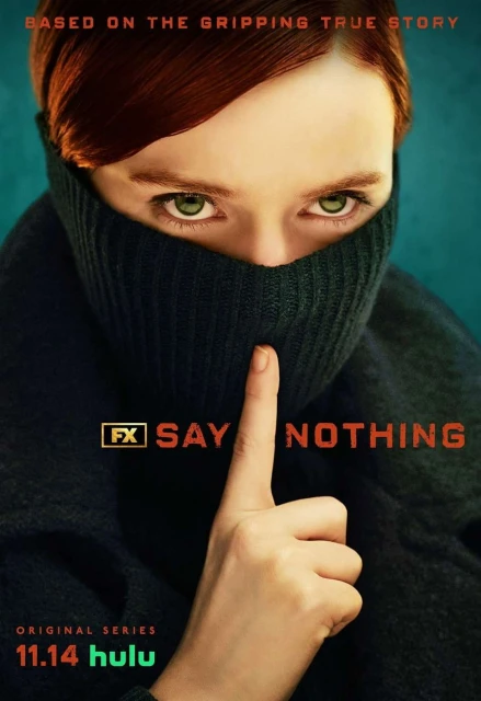 Close-up of a woman with red hair wearing a black turtleneck covering her mouth and nose, holding a finger to her lips in a studio shot.