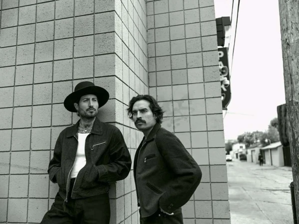Two men standing against a tiled exterior wall on a street corner, captured in monochrome by photographer Kurt Iswarienko.