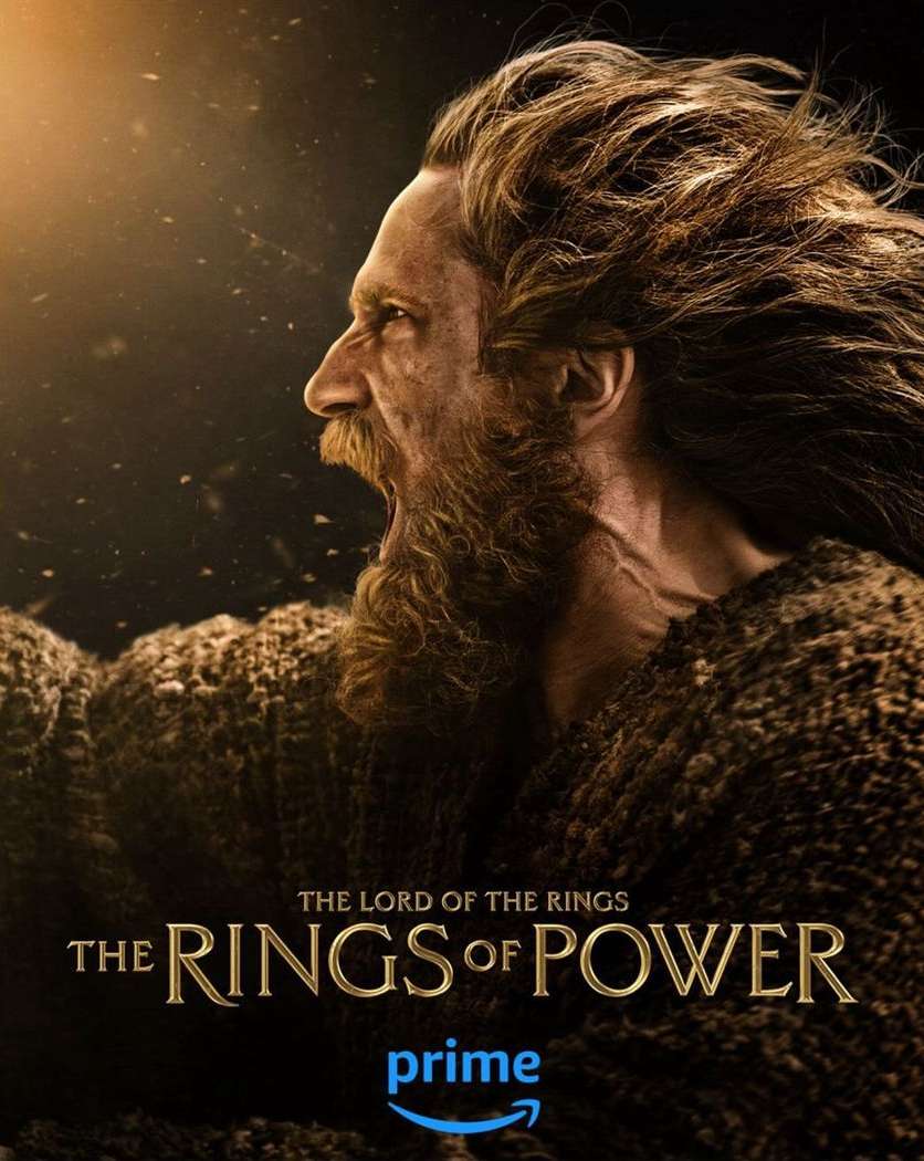 Profile shot of an adult male with long brown hair and beard in a brown robe, against a dark background, for The Rings of Power.