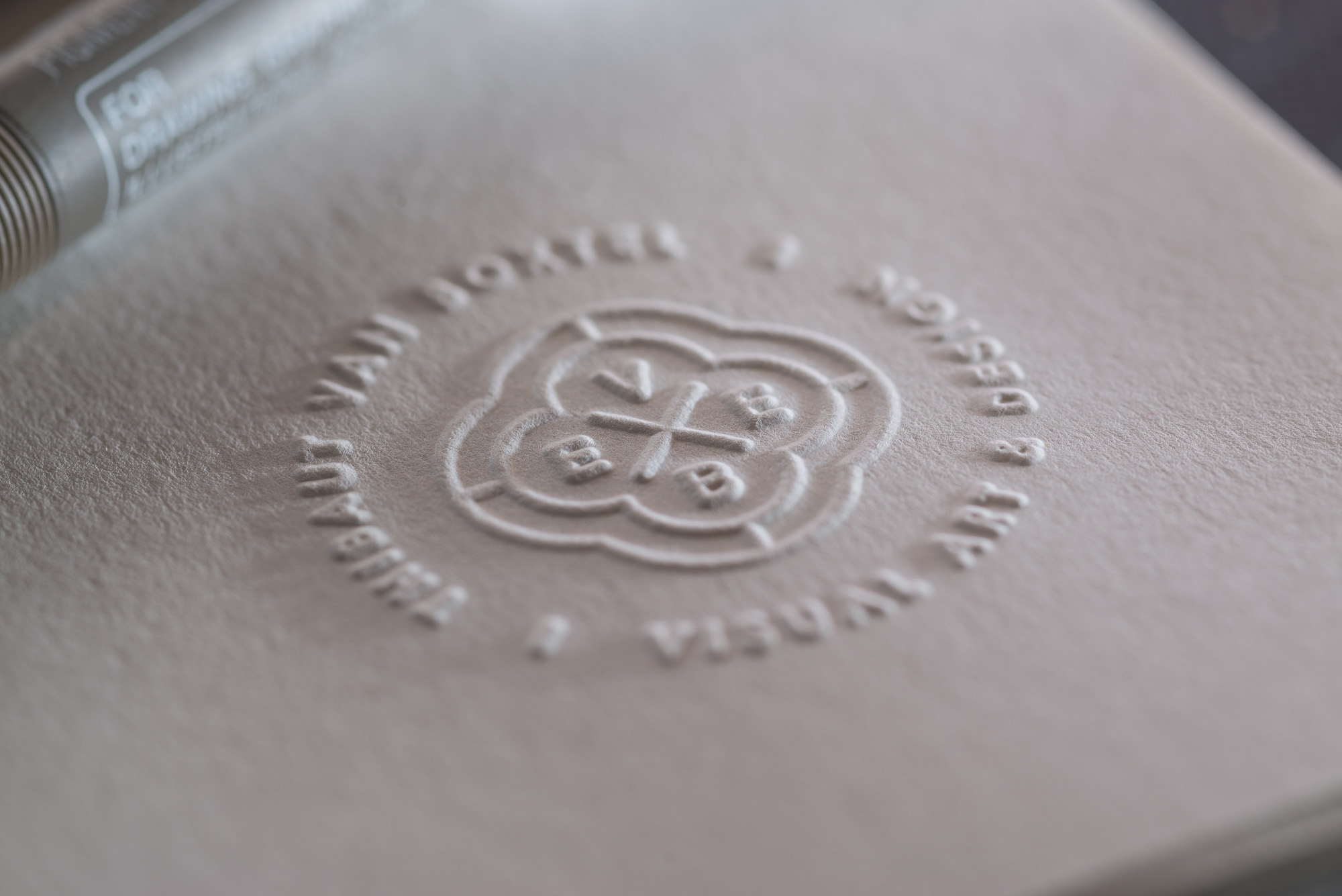 Close-up of an embossed logo on textured paper with visible brand initials and surrounding text, soft lighting, studio environment.