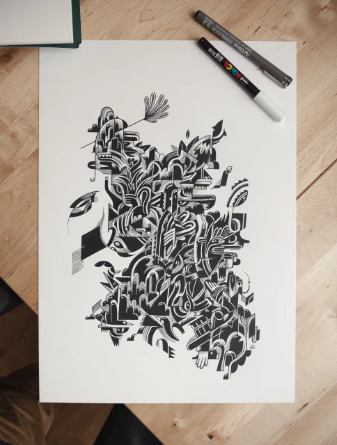 Abstract ink drawing on paper featuring a complex composition of black and white shapes and lines. The artwork has two pens nearby.