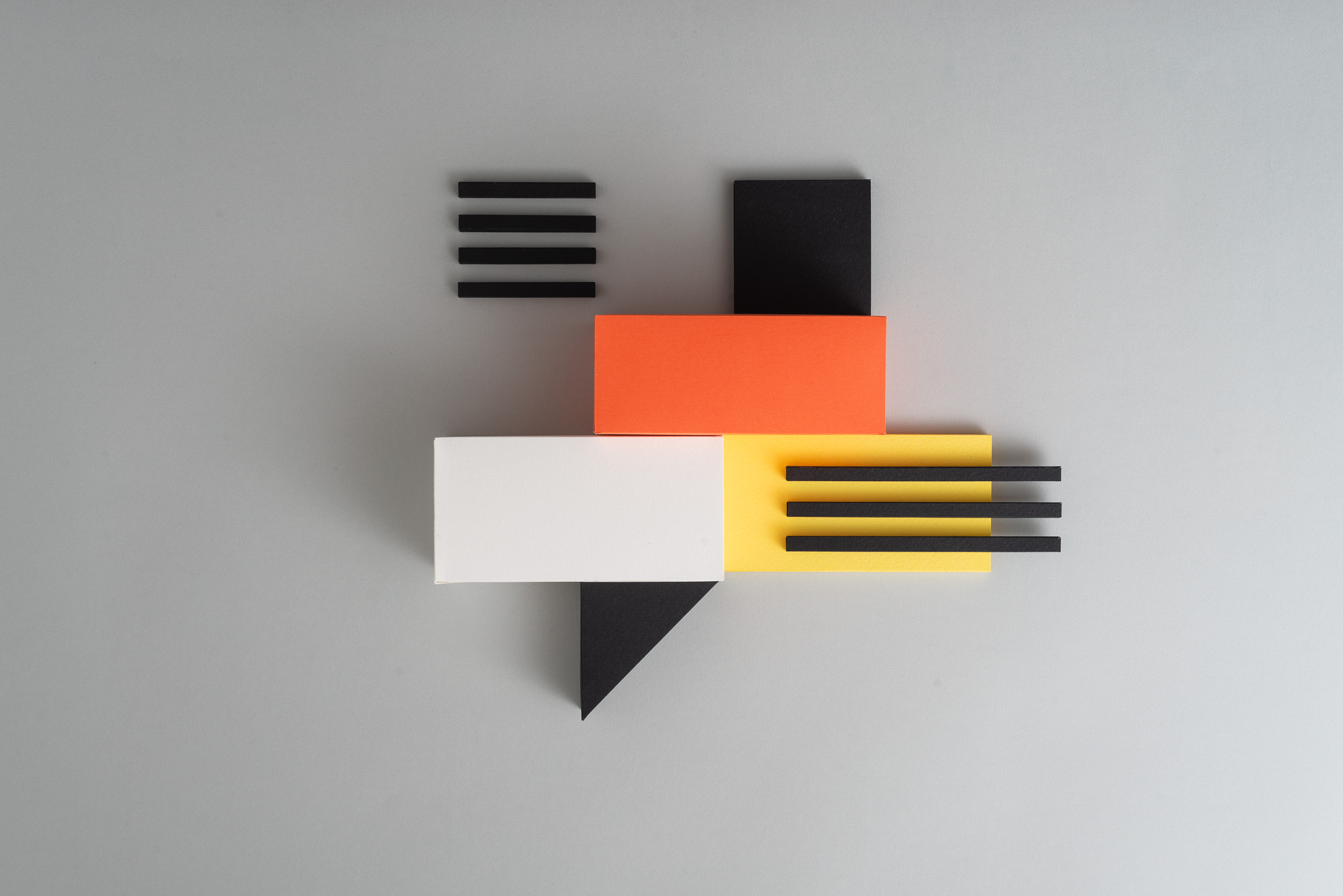 Abstract geometric composition with rectangles, squares, triangles in orange, yellow, white, and black on gray background.