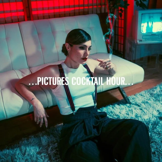 Stylish woman in wide-leg pants and suspenders poses indoors with a cigarette, sitting near a white couch and vintage TV set.