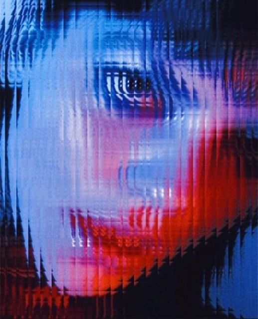 Abstract portrait of a face with distorted vertical lines in shades of blue and red, creating a textured and blurred effect.