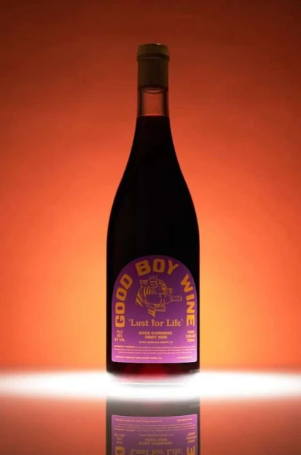 Wine bottle with purple label on a reflective surface against an orange background, showcasing wine product photography.