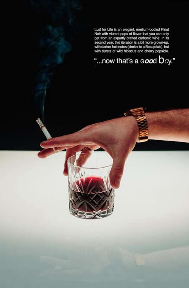 Person's hand holding patterned glass of red liquid, cigarette in hand, gold watch visible, set against black and white backdrop.