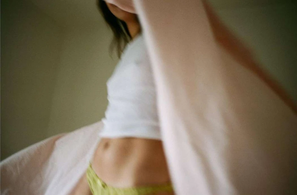 Woman in a white top and yellow bottoms standing indoors with blurred fabric in the foreground.
