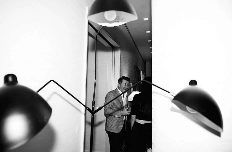 Indoor shot of a man in a patterned blazer talking to a woman, with modern black lamps in a monochromatic setting.