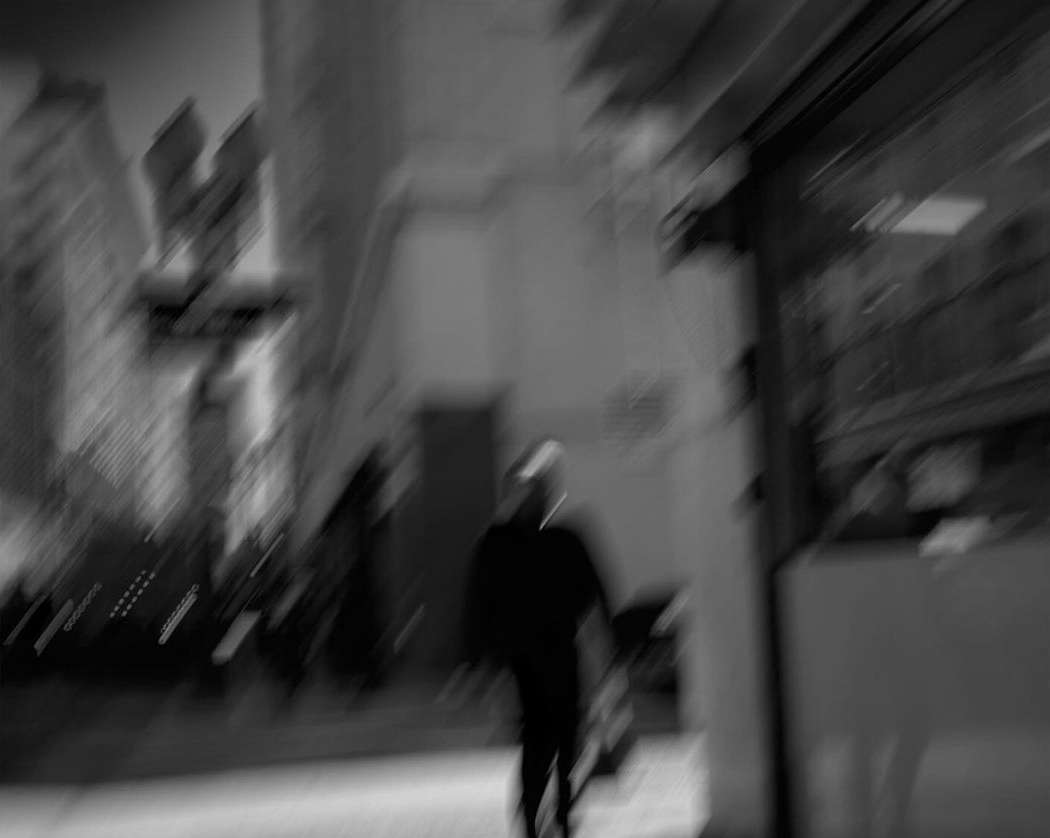Monochrome motion-blurred urban street scene with a silhouetted figure walking past buildings