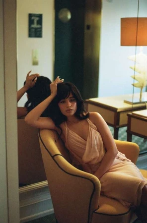 Woman in pink dress seated in a yellow armchair, reflected in a mirror inside a hotel room by Erica Hernandez