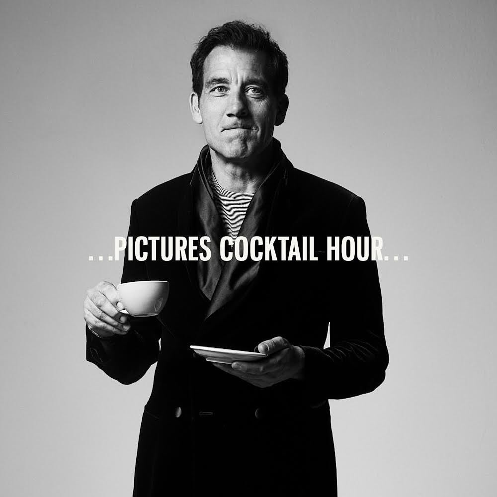 Black and white portrait of Clive Owen holding a teacup and saucer in a dark coat, against a light background.