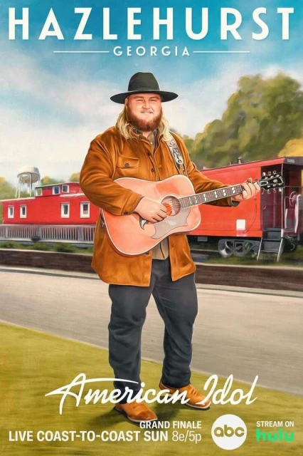 A male performer with an acoustic guitar stands in front of a train car, promoting American Idol in Hazlehurst, Georgia. Grand finale event.