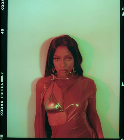 Woman in a metallic dress with gold jewelry posing in front of a green and white wall in a portrait photograph with studio lighting.